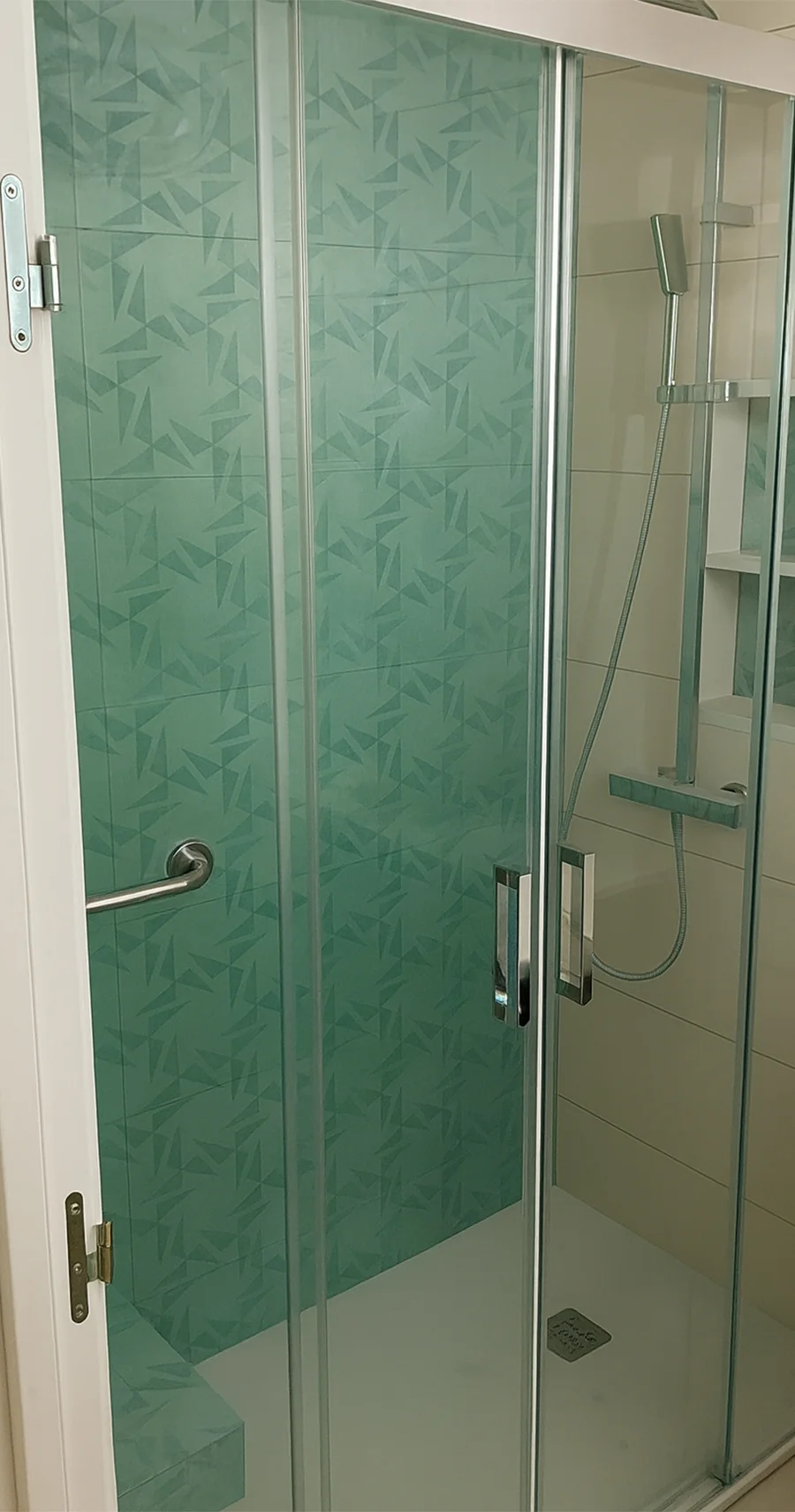 Ducha moderna con mampara de vidrio, azulejos verdes con diseño geométrico y grifería de acero inoxidable. Cuenta con nicho empotrado y plato de ducha blanco. Foto de reformas de baños en Las Palmas.
